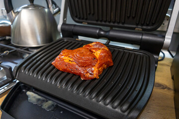 Grilled marinated meat cooking on an electric contact grill in a modern kitchen.