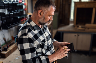 Male carpenter using digital tablet in workshop, checking project plans or measurements.