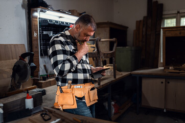 Male carpenter using digital tablet in workshop, checking project plans or measurements.