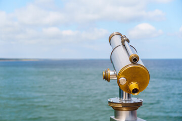 Public telescope on the coast provides a clear view of the ocean under a partly cloudy sky allowing for travel planning and observing the horizon from the viewpoint