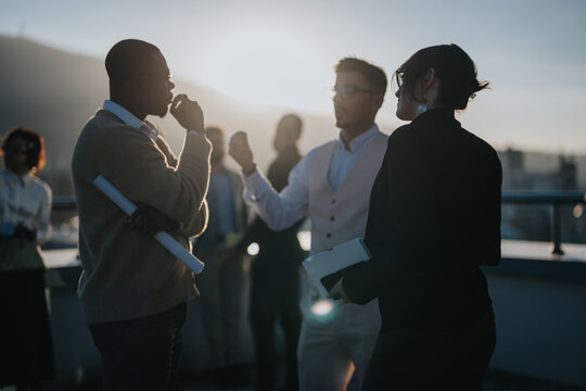 A group of multiracial business colleagues engaged in a brainstorming session on a rooftop at sunset, promoting teamwork and innovation. The scene embodies diversity and dynamic collaboration.