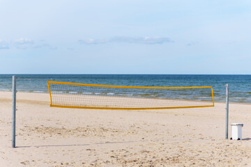 Beautiful summer day on an empty beach with golden sand shows a volleyball net ready for a game with the blue ocean and sky offering a scenic sports beach vacation scene