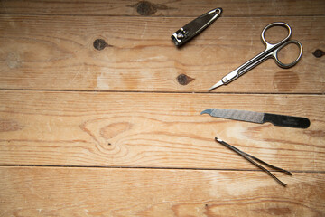 Nail grooming tools&mdash;file, scissors, clippers, tweezers&mdash;neatly arranged on a wooden slatted background, top-down view.