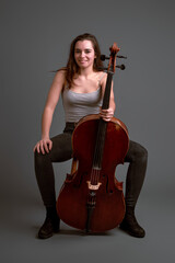 Young female cellist posing with her instrument on gray background