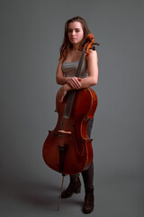 Young musician posing with cello on gray background