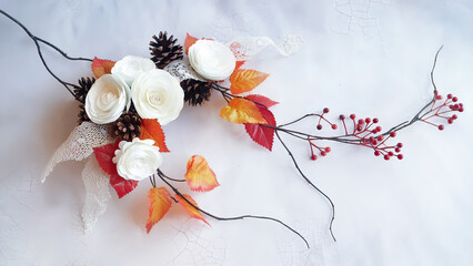 Artistic arrangement featuring white paper flowers pinecones and autumnal leaves on white background