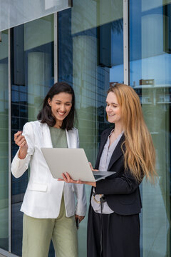 Business meeting outdoors with two professional women in their 30s of different ethnicities discussing ideas using a laptop in an urban setting