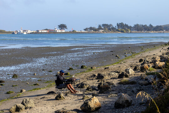 A man with a laptop working on a beach or bay at low tide.  Full-time RV nomad lifestyle, working in shorts from his home office.