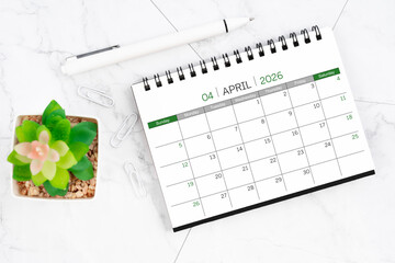 Desk calendar on month of April 2026 with pen on white marble background.