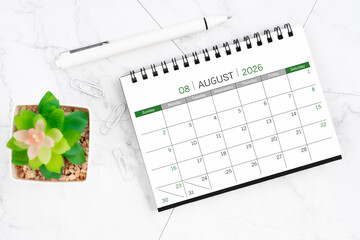 Desk calendar on month of August 2026 with pen on white marble background.