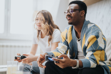 A smiling couple focused on playing a video game, holding controllers, sitting in a well-lit living...