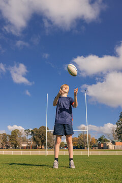 Junior rugby union player standing on field handling ball with goal posts in background