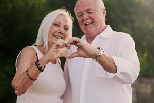 An elderly couple forms a heart with their hands