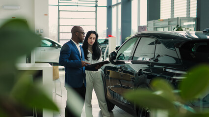 African-American car salesman signs a contract with a woman to sell a new car at a car dealership....
