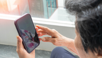 Asian elderly woman using a smartphone interacts with the screen attentively, reflecting the growing connection between seniors and digital technology.