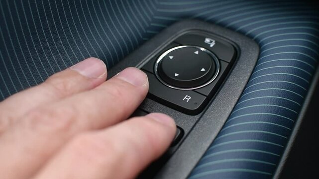 Driver's hand confidently adjusts side mirrors using modern electronic controls, highlighting intuitive interface and comfort in car interior.
