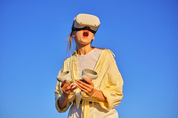 Enthusiastic woman enjoying virtual reality gaming outdoors under clear blue sky