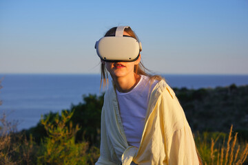 Woman immersed in virtual reality with headset outdoors at sunset