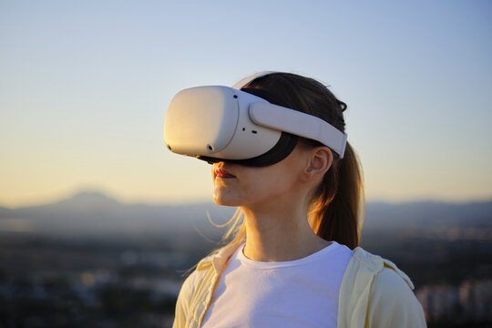 Woman experiencing virtual reality outdoors at sunset with headset
