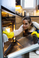 Woman cleaning oven in modern kitchen while wearing yellow gloves