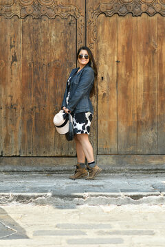 Chica latina usando un vestido de pie frente a una puerta de madera en la ciudad de Antigua Guatemala. Toma Vertical.