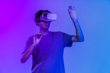 One young african american boy wearing VR glasses over pink background in neon light. Youth and virtual lifestyle of future. Concept of games, digitalization and technology.
