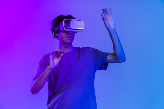 One young african american boy wearing VR glasses over pink background in neon light. Youth and virtual lifestyle of future. Concept of games, digitalization and technology.