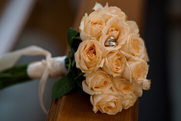 Wedding Rings on Bouquet of Peach Roses Close-up, Romantic Celebration, Ceremony Detail, Soft Lighting, Floral Arrangement.