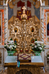 Fototapeta premium Orthodox Church Altar: Golden Iconostasis, White Flowers, Candles, Books Religious Ceremony Setting Inside a Beautiful Eastern Christian Temple