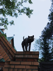 Fototapeta premium Metal statue figurine cat on the brick wall of the house. Summer twilight.