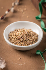 Fennel seeds in a white bowl on a textured brown surface with a delicate feather and blurred plant stem in the background