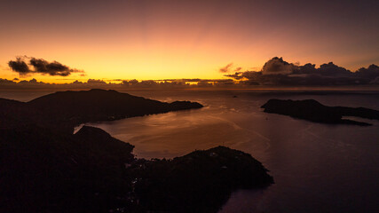A fiery sunset bathes the horizon in warm light, while the islands and water rest in shadows. Praslin, Seychelles.