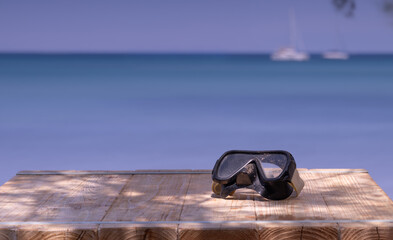 Summer vacation themed background - sandy snorkeling mask on a wooden table with sea in the background