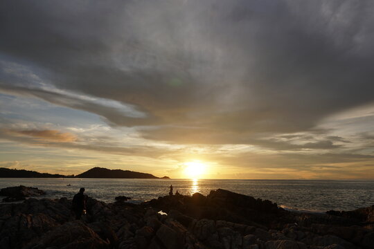 Serene Sunset Over Rocky Coastline With Silhouetted Figures Against Vibrant Sky Colors