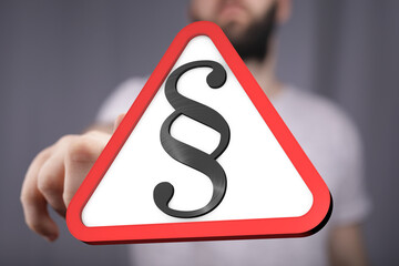 Stock photo of a hand pointing at a warning sign with a paragraph symbol.  Ideal for legal, law,...