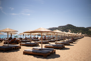 Neatly arranged wooden sun loungers with straw parasols on a sandy beach