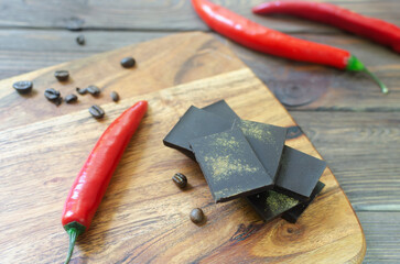 Pieces of extra dark chocolate with three red chili peppers on a wooden cutting board on the table. Trend food concept. Selective focus. Horizontal orientation