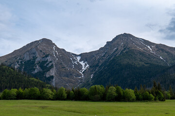 Fototapeta premium Panoramic view of the High Tatras above the village of Ždiar, Slovakia, with green meadows, forests, and ski lift structures under a clear spring sky.