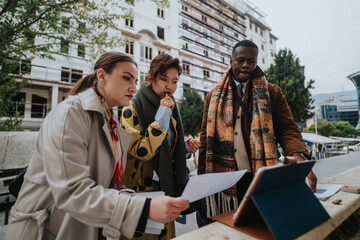 A group of young adults, dressed formally, reviewing documents and using a tablet, symbolizing teamwork, decision-making, and collaboration in a professional context.