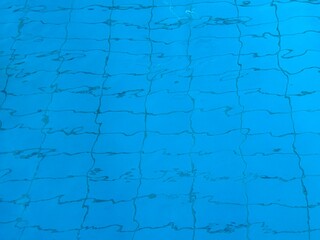 Rippling blue water in swimming pool with blurry tile pattern at the bottom. Horizontal picture.