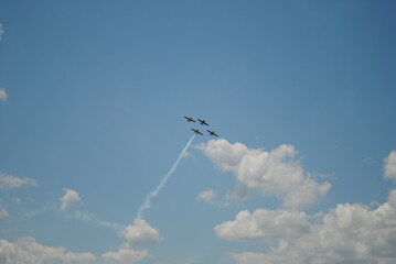 Four airplanes flying in formation leaving a smoke trail against a blue sky with scattered clouds