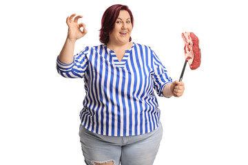 Naklejka premium Overweight woman holding a raw meat steak and gesturing ok sign