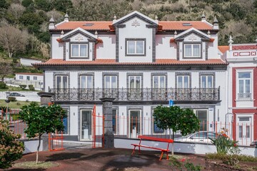 Elegant White Building Facade With Red Roof And Lush Hillside Background. Traditional Azorean Portugese architecture, ornate balconies, tranquil garden, scenic landscape