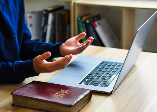 Christian online technology concept. Hands praying of christian with digital computer laptop, Online live church for sunday service. Asian catholic man are reading Holy bible book and online study.