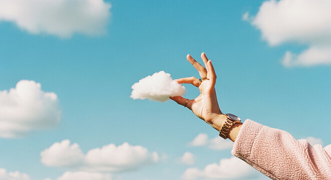 Woman's hand holding a small cloud against a blue sky