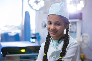 Preteen Asian girl standing in surgical suite wearing cap and coat holding stethoscope, copy space