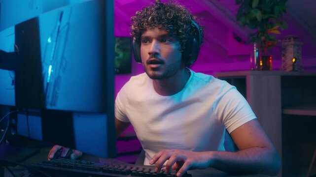 Concentrated happy Arabian Indian Muslim man typing code keyboard computer games playing video game cyber sport male excited guy gamer streamer win success winning online player achieve enjoy studio