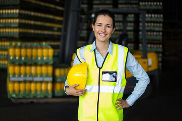 Female warehouse supervisor standing in storage wearing safety vest holding hardhat with forklift © wavebreak3