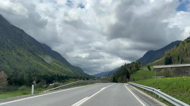 Traveling. Point of view in a car moving on a road in mountains. Drive in Alps with cloudy sky at the background.