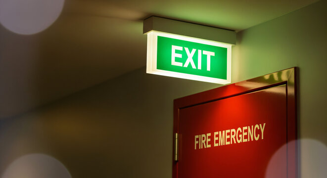 Green exit sign illuminated above a red fire emercency doorway. The scene suggests an emergency exit area within a building.